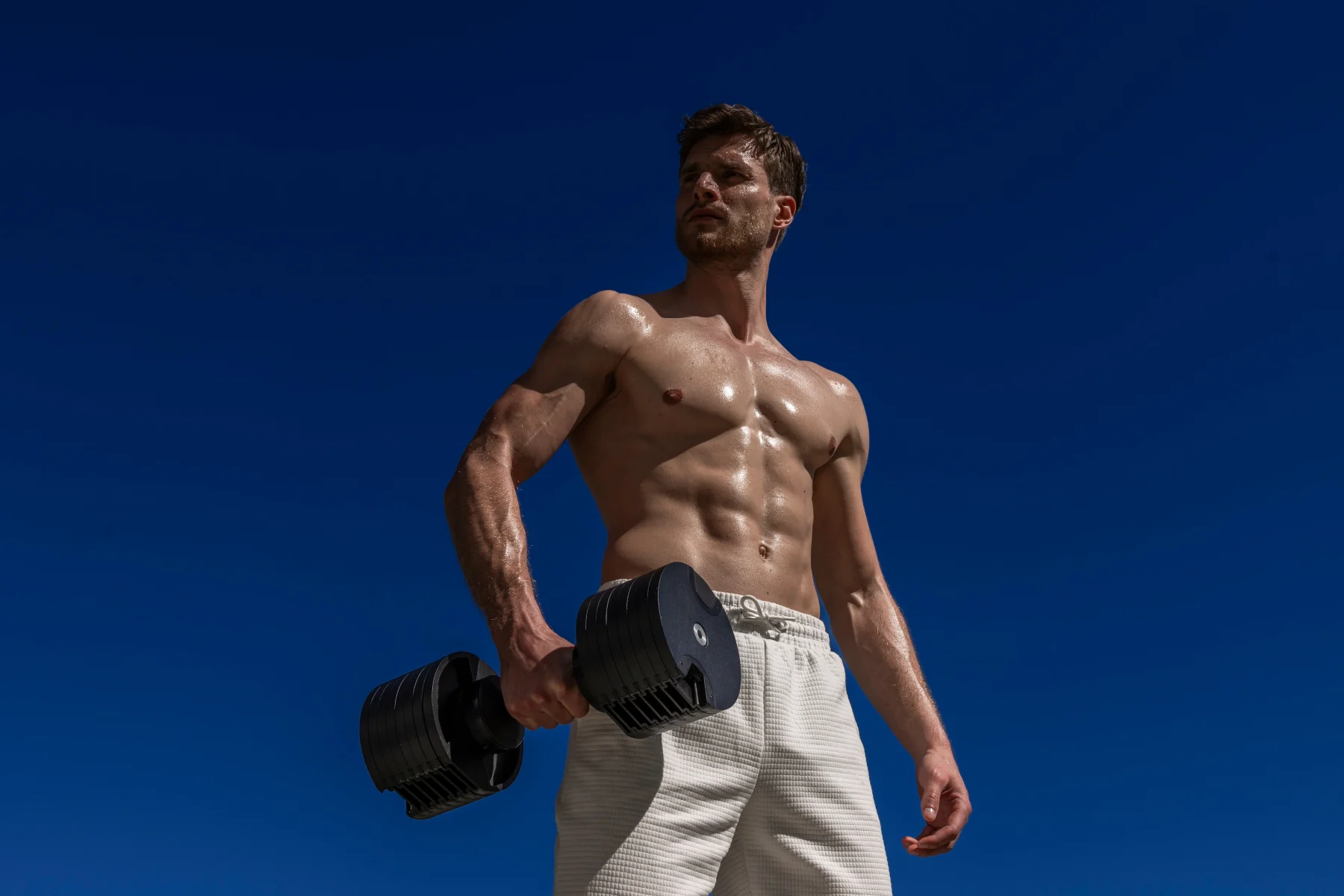 An athlete carrying a NÜOBELL adjustable dumbbell against a blue sky.