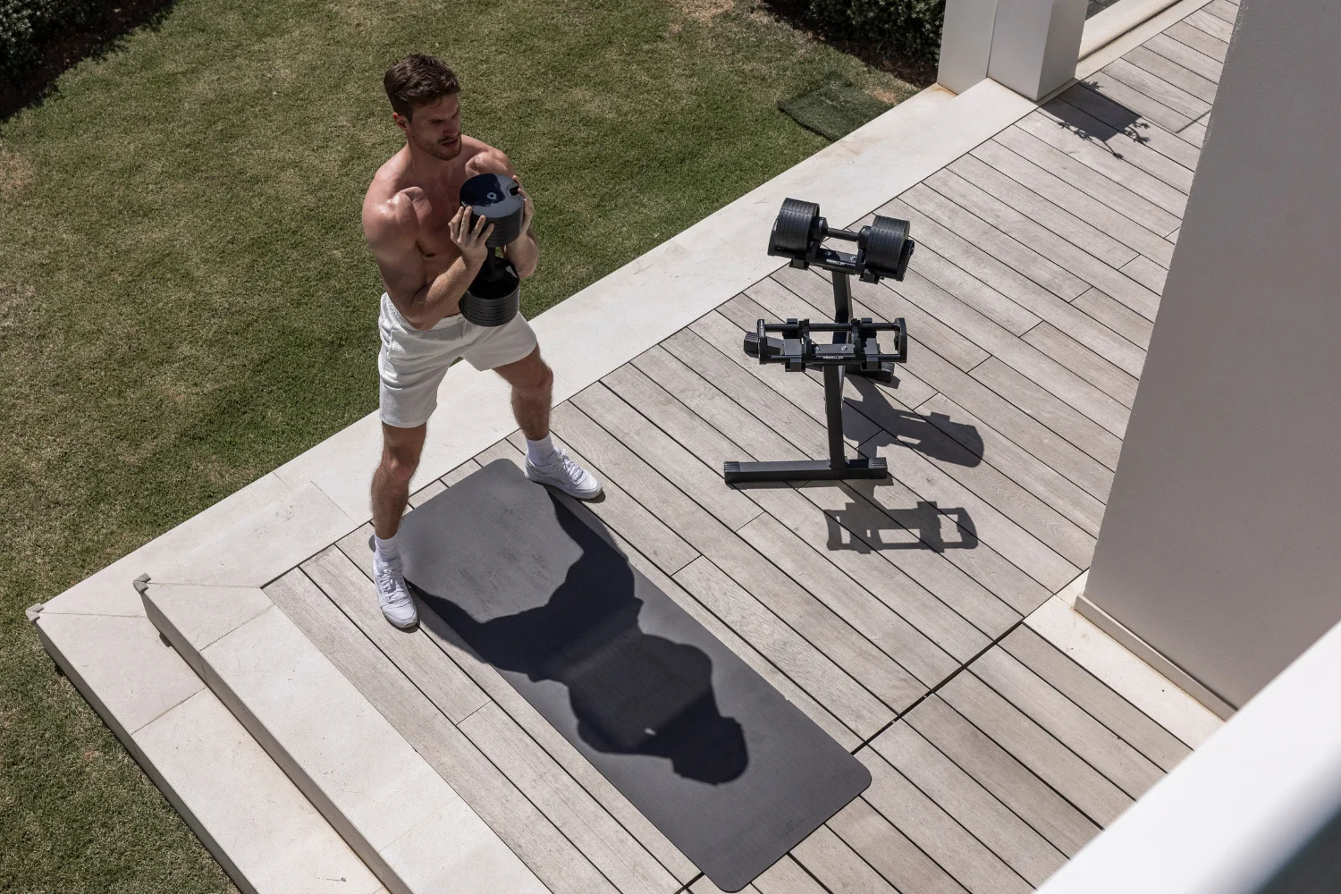 An athlete training beside NÜOBELL adjustable dumbbells on a floor stand.